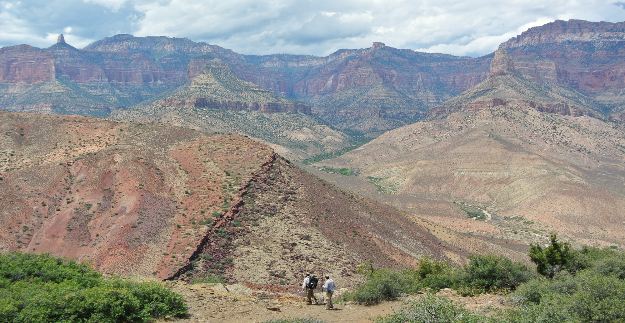 Photo showing two small figures in the foreground in front of large rocky landscape in the Grand Canyon.